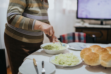 A senior woman arranging a meal on a table with salad and bread in a homely setting. The scene showcases domesticity, care, and preparation for dining.