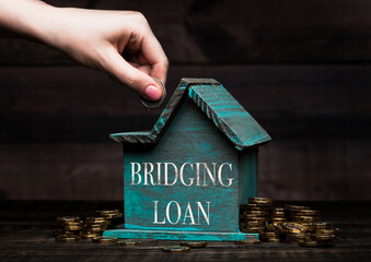 Wooden house model with coins next to it and hand