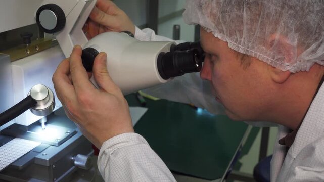 Laboratory researcher checks quality of manufactured microchips using microscope. Final stage of semiconductor transistor production. High-precision equipment and nanotechnology in modern industry.