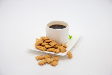 Coffee cup with crispy pillow cookies scattered on plate on white background