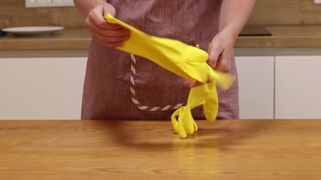 A woman in an apron and yellow gloves wipes the table with a viscose napkin from dust and dirt. Cleaning in the apartment. Cleaning service. Close-up of hands in cleaning gloves. Cleaner
