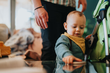 A curious baby touches a tabletop while being attentively supervised in a comfortable home setting,...