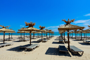 Empty beach with parasols and chaise longues by the sea at resort on sunny summer day