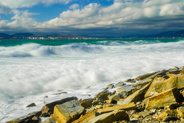Kabardinka resort. Large green storm waves in white foam. In background is port of Novorossiysk and...