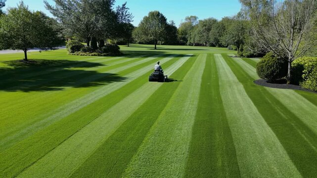 A person on a riding lawn mower creates perfect stripes on a huge green lawn this meticulous landscaping shows order precision professional care a beautiful maintained property
