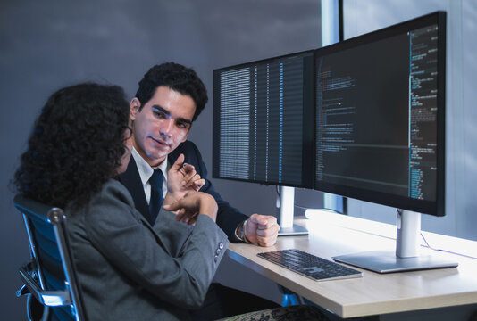 Man and woman team business professional formal attire collaborate desk with dual monitor computer talk about financial stock market in modern office highlight teamwork technology, professional work