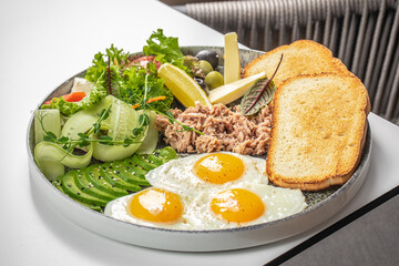 Breakfast plate with fried eggs, tuna, avocado, toast, cheese, and fresh vegetables