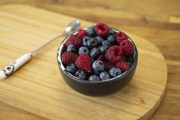 ceramic breakfast bowl with blueberries and raspberries with spoon in the distance on wooden steel