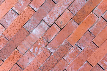 A close-up view of a herringbone pattern made of red bricks. Bricks are arranged in a diagonal...