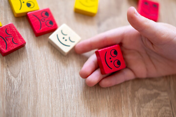 Wooden blocks with emotions, Child's hand playing with wooden blocks, emotional intelligence in...