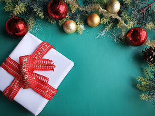 white gift with red ribbon and gold and red Christmas ornaments on a green background with space for text
