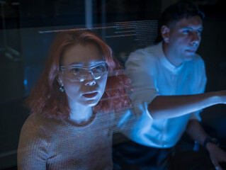 Man and woman team member collaborate on working digital project with code display on transparent...