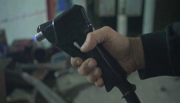 A hand holds a black tool with a blue flame