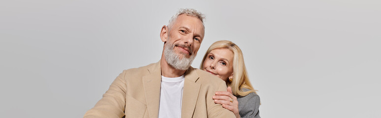 Joyful senior couple sharing a tender moment in stylish outfits against a neutral background