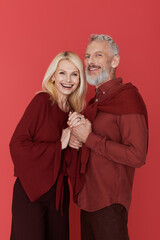 Charming senior couple embraces love in stylish attire against a vibrant red backdrop