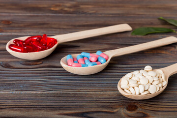 Vitamin capsules in a spoon on a colored background. Pills served as a healthy meal. Red soft gel...