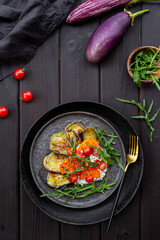 Salad with fried eggplant, cream cheese, tomatoes and arugula on dark background top view vertical photo. Vegetarian food
