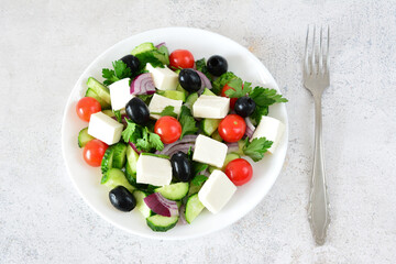 Fresh and Colorful Greek Salad on a White Plate with cherry tomatoes and a fork