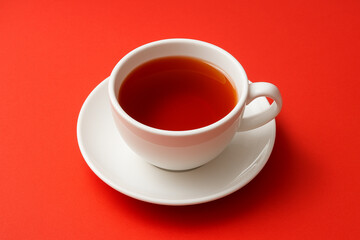Cup of brewed black loose leaf tea, aromatic traditional beverage on red background