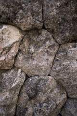A close-up, detailed texture of a rustic stone wall. A natural background of large, rough, gray rocks fitted together.
