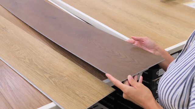 Woman choosing dark wooden laminate flooring panel in hardware and home decor store