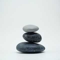 Three smooth stones are stacked in a balanced pyramid against a neutral backdrop, conveying simplicity and tranquility.