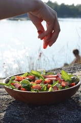 Hand adding fresh strawberries to summer salad outdoors
