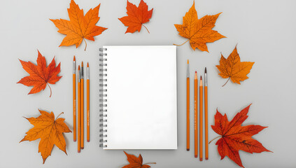 “Blank White Spiral Sketchbook with Paintbrushes, Pencils, and Autumn Leaves – Minimalist Art Workspace Flat Lay”
