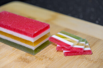 Colorful multi-layered gummy candy block and sugar-coated sweet slices displayed on a rustic wooden...