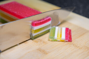 A sharp knife carefully slicing vibrant layered agar-agar jelly on a wooden cutting board,...