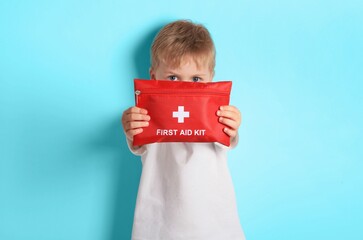 Child holds a bright red first aid kit against a light blue background 