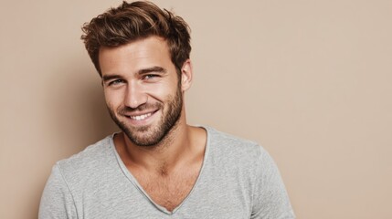 Fototapeta premium Smiling young man with a beard and casual grey t-shirt posing against a beige background.