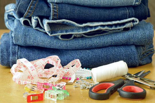 Professional tailoring supplies with folded denim jeans, measuring tape and sewing tools on wooden table. Fashion alteration, clothing repair, DIY crafting workspace, zero waste and handmade design