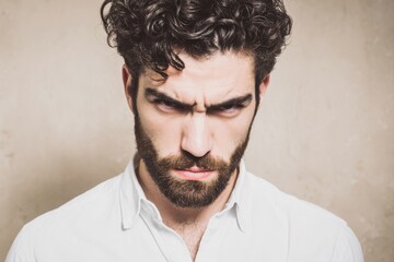 Close-up of a frustrated young man with curly hair and a beard expressing annoyance.