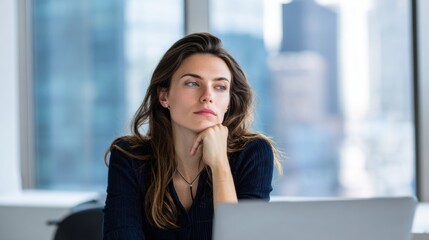 Thoughtful young woman sitting at desk in modern office with city view atmosphere.