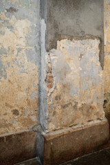 A closeup image showcasing a detailed view of a weathered wall with peeling paint and exposed mortar, highlighting its textured and aged appearance.
