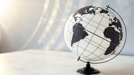 Minimalist black and white world globe on desk illuminated by sunlight showing continents and grid lines perfect for geography education, classroom materials and creative global background designs