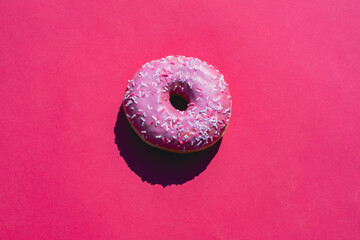 A fresh donut with a smooth pink icing and colorful sprinkles sits centered on a bold red...