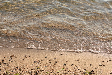 Medium shot of the seaside: waves touching the sandy shore. Summer atmosphere of relaxation and peace.