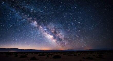 Fototapeta premium Milky Way stretches across dark desert sky, faint horizon glow below