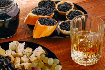 An exquisite spread featuring caviar on toasted breads, gourmet cheeses, and a glass of whiskey,...