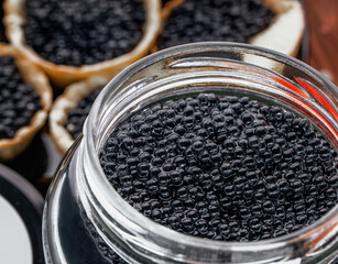 Delicious black caviar is being carefully scooped from a sleek container, showcasing its rich texture and color. The scene highlights the luxury of fine dining and gourmet cuisine.