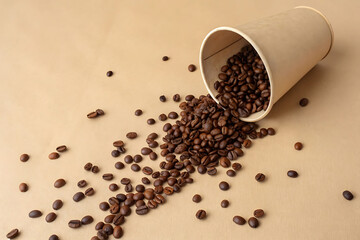 Roasted coffee beans spreading from a brown paper cup isolated on white background.