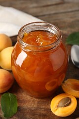 Tasty apricot jam and fresh fruits on wooden table, closeup