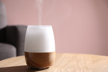 One stylish aroma lamp on wooden table against pink wall, closeup. Space for text
