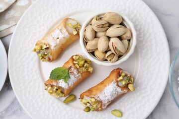 Delicious cannoli with cheese, pistachios, powdered sugar and mint on white marble table, top view