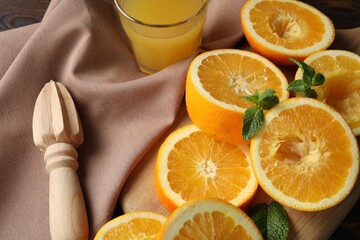 Freshly squeezed orange juice, fruits, mint, juicer and towel on wooden table, closeup