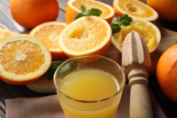 Freshly squeezed orange juice, fruits with mint, juicer and towel on table, closeup