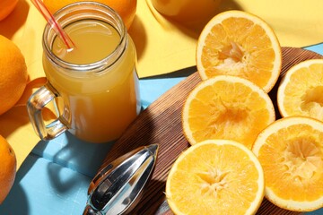 Freshly squeezed orange juice, fruits and juicer on blue wooden table, closeup