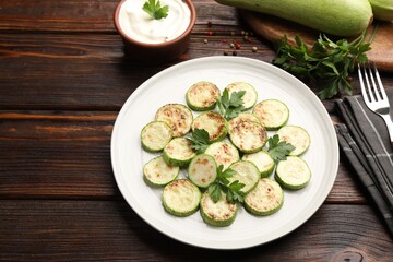 Delicious fried courgette slices with parsley served on wooden table, closeup